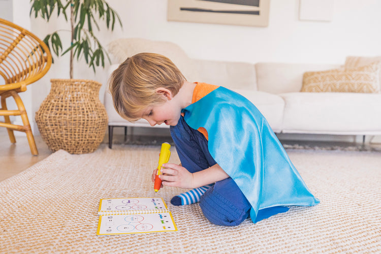 A child in a cape interacting with the Numberblocks Hot Dots 11-20 Activity Book & Interactive Pen